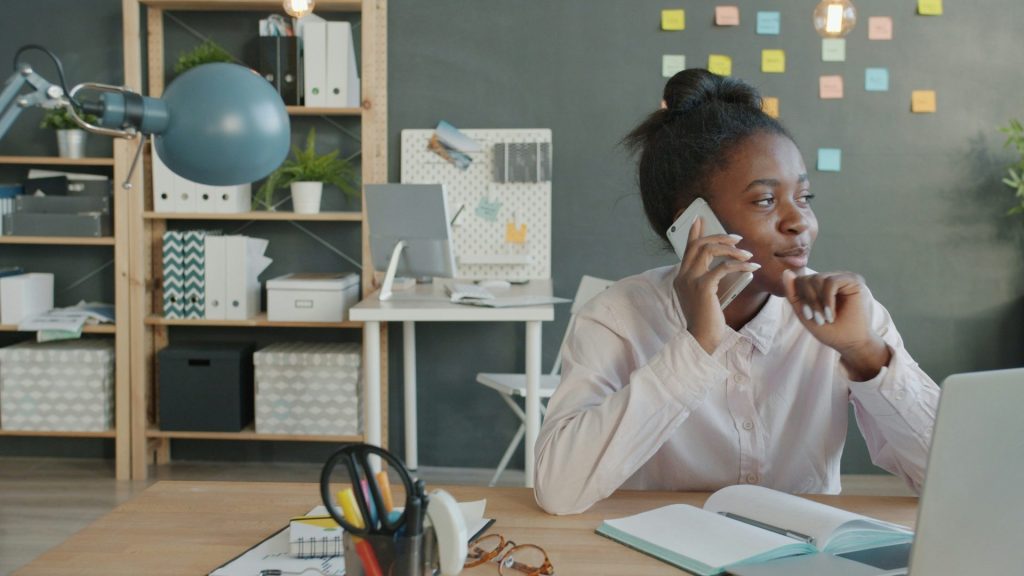 Woman talking on phone at desk in office.