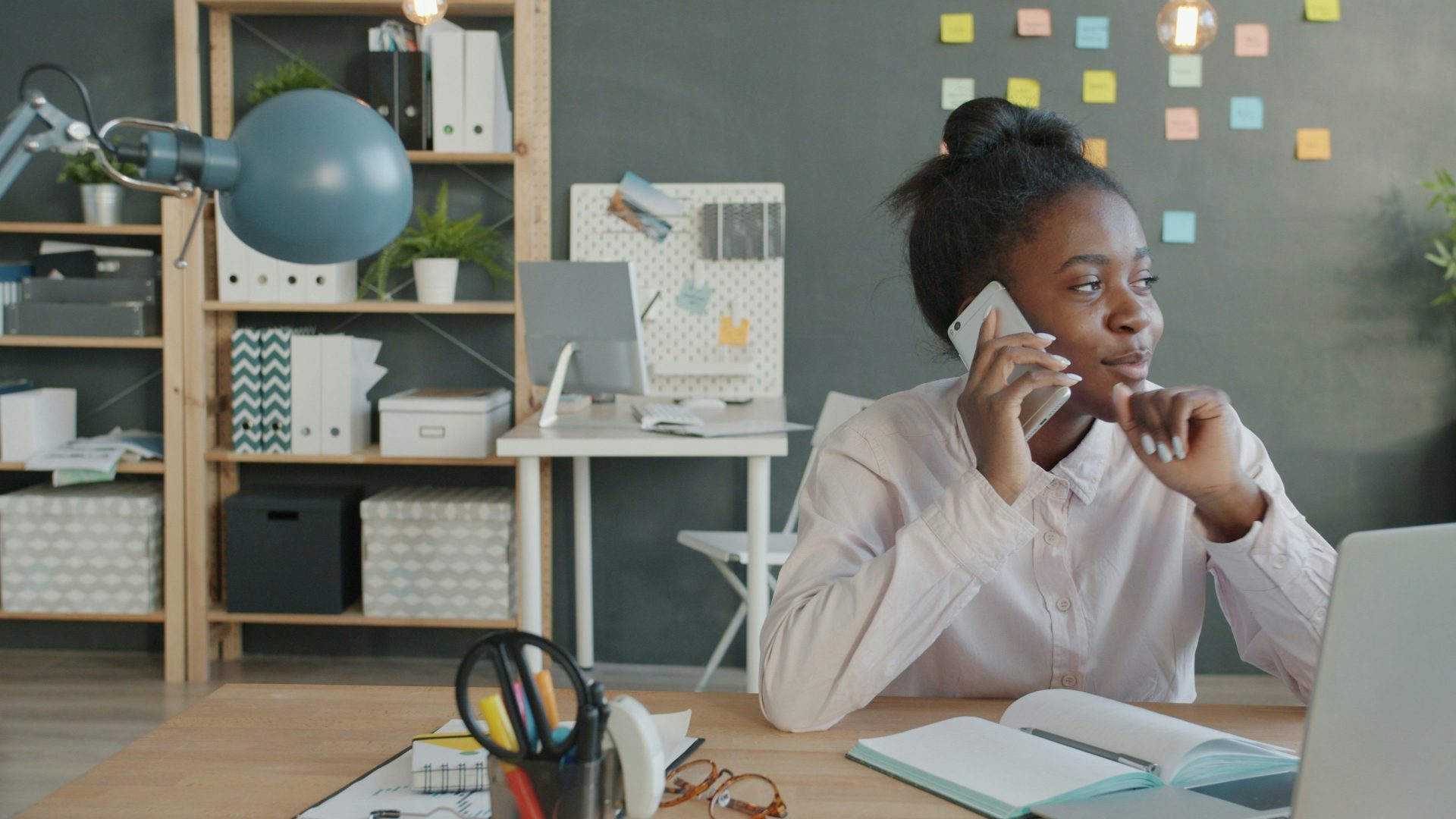 Woman talking on phone at desk in office.
